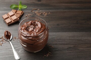 Delicious chocolate pudding in glass and spoon on wooden table, closeup. Space for text