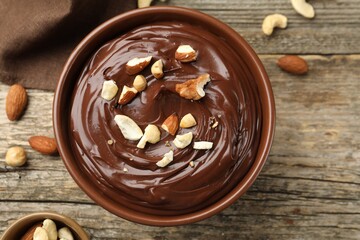 Delicious chocolate pudding with nuts in bowl on wooden table, flat lay