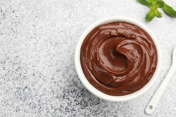 Delicious chocolate pudding in bowl and mint on light grey textured table, flat lay. Space for text