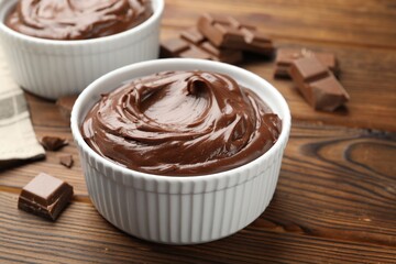 Tasty pudding in bowls and pieces of chocolate on wooden table, closeup