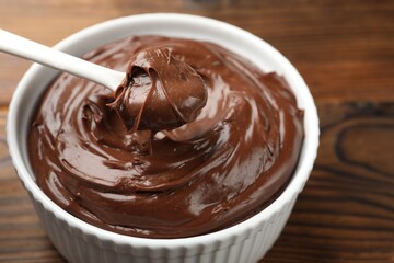 Taking tasty chocolate pudding from bowl with spoon on wooden table, closeup