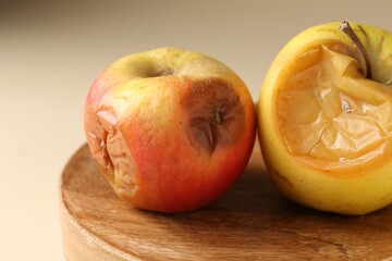 Two rotten apples on beige background, closeup