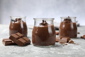 Tasty pudding in glass jars and pieces of chocolate on light grey table, closeup