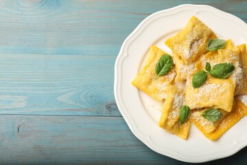 Delicious ravioli with cheese and basil on light blue wooden table, top view. Space for text