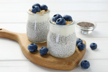 Delicious pudding with chia seeds, yogurt, blueberries and granola in glasses on white wooden table, closeup. Superfood