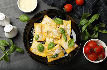 Delicious ravioli with parmesan cheese and basil on black table, flat lay