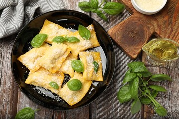 Delicious ravioli with parmesan cheese and basil on wooden table, flat lay