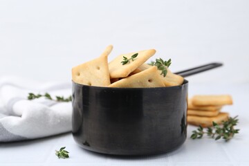 Tasty salty crackers and thyme on white tiled table, closeup