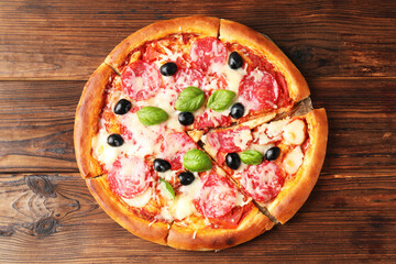 Tasty pizza with salami, cheese, basil and olives on wooden table, top view