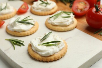 Tasty crackers with cream cheese, rosemary and tomatoes on white table, closeup