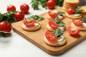Tasty crackers with cream cheese, tomatoes and parsley on white table, closeup