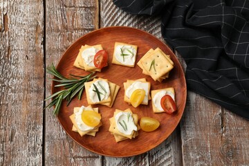 Tasty crackers with cream cheese, rosemary and tomatoes on wooden table, top view