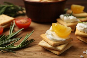 Tasty crackers with cream cheese, rosemary, salt and tomatoes on wooden table, closeup