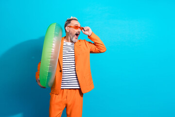 Trendy middle aged man in orange suit with inflatable ring on vibrant blue background, embodying...