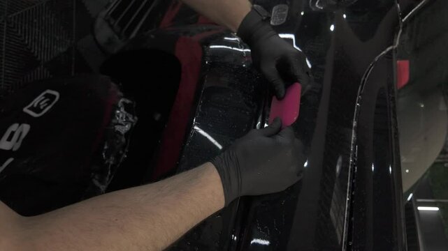 Squeegeeing while applying PPF (paint protection film) to a black truck at an automotive detailing shop. Ungraded D-Log M footage.