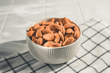 Shelled almonds are piled high in a small white bowl resting on a checkered cloth, creating a simple yet appealing image of healthy snacking