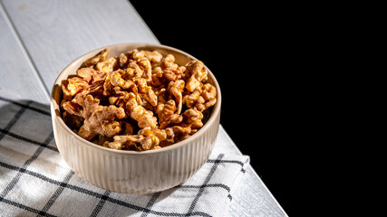 Shelled walnuts resting in a bowl on a checkered tablecloth create an inviting scene, complemented by a dark background that enhances the natural textures and colors