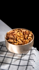 Shelled walnuts resting in a bowl on a checkered tablecloth create an inviting scene, complemented by a dark background that enhances the natural textures and colors