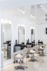Row of modern styling chairs and mirrors in a hair salon interior, featuring professional tools and...