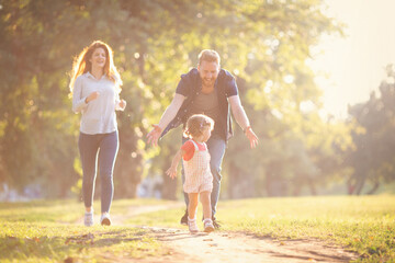 Fototapeta premium Young happy parents with their baby girl having fun outdoors