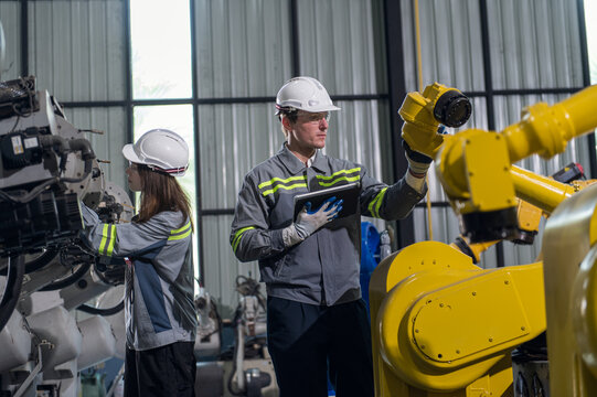 Engineer standing by robotic arm and operating machine in industry factory, technician worker check for repair maintenance electronic operation