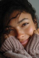 A beautiful woman with brown eyes and a warm smile holds her face in her hands.