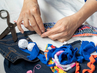 Reusing denim..A close-up of skilled female hands knitting a colorful rug from scraps of used fabric. Authentic folk art