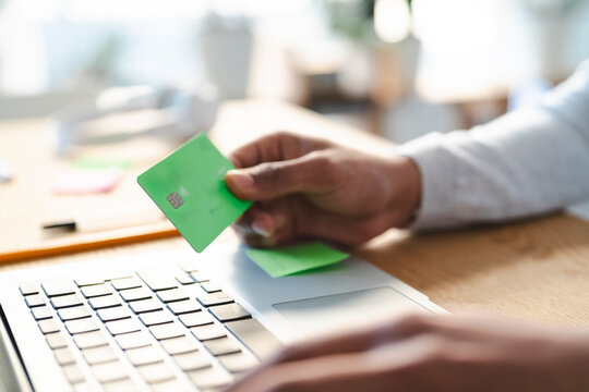 An Arab young man is using a credit card to make an online purchase. He is typing on his laptop to complete the transaction.