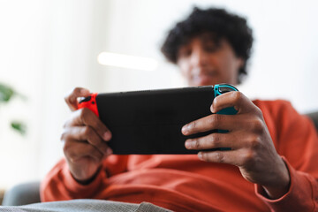 An Arab young man is playing a handheld video game console. He is relaxing at home, enjoying his leisure time.