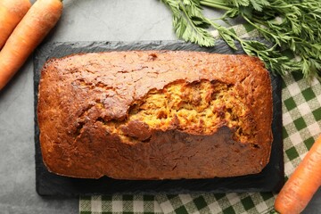 Tasty carrot cake and vegetables on grey textured table, flat lay