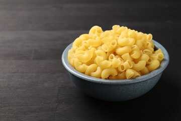 Raw horns pasta in bowl on dark wooden table, closeup. Space for text