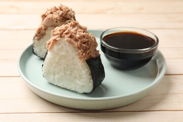 Tasty onigiri (Japanese rice balls) with tuna and soy sauce on wooden table, closeup