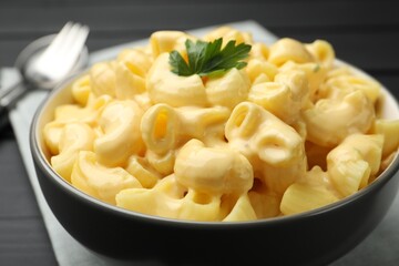 Delicious macaroni and cheese with parsley served on black wooden table, closeup