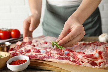 Woman putting rosemary onto raw pork ribs at table, closeup