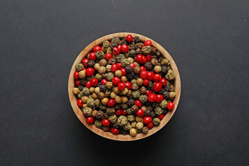 Aromatic peppercorns in bowl on dark table, top view