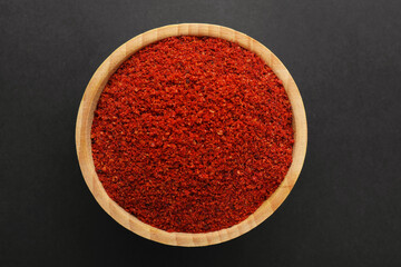 Red pepper powder in bowl on black background, top view. Aromatic spice