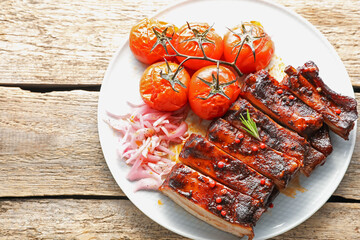 Delicious pork ribs, sun dried tomatoes and onion on wooden table, top view. Space for text