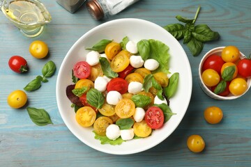 Tasty salad with yellow tomatoes, basil and mozzarella cheese on light blue wooden table, flat lay