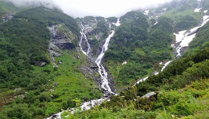 Un majestuoso paisaje monta&ntilde;oso captura la serena belleza de las cascadas que se desbordan por exuberantes laderas verdes. El agua centellea al caer sobre acantilados rocosos, rodeados de densa vegeta