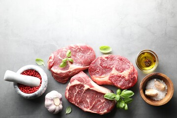 Pieces of raw beef meat and spices on grey table, flat lay. Space for text