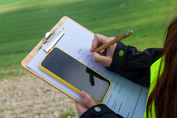 Agricultural engineer writing notes on clipboard and using mobile phone in a field of wheat