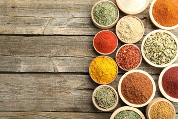 Different aromatic spices in bowls on wooden table, flat lay. Space for text