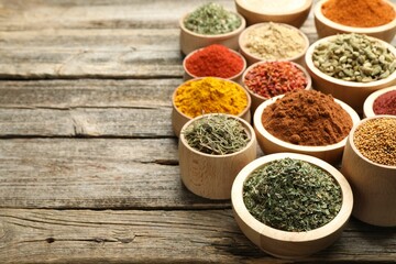 Different aromatic spices in bowls on wooden table, closeup. Space for text