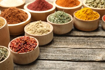 Different aromatic spices in bowls on wooden table, closeup. Space for text