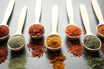 Many different spices in spoons on grey table, closeup