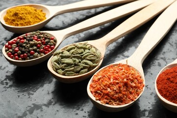 Many different spices in spoons on black table, closeup