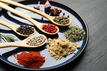 Different aromatic spices in spoons on black table, closeup