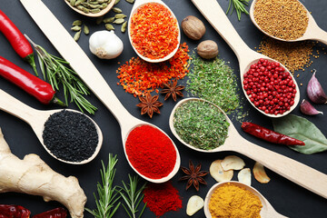 Different aromatic spices in spoons on black table, flat lay