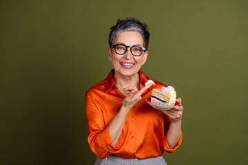 Charming mature woman holding a slice of colorful cake in a festive mood, showcasing her vibrant personality