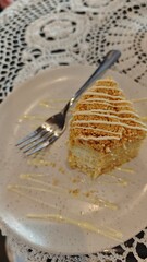 Slice of layered honey cake with cream and crumbs served on a plate with a fork. Concept of dessert indulgence, homemade sweetness and cafe culture